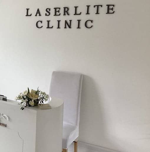 The clinic's reception, with LASERLITE CLINIC lettering on the wall, a white chair and flowers The clinic's reception, with LASERLITE CLINIC lettering on the wall, a white chair and flowers
