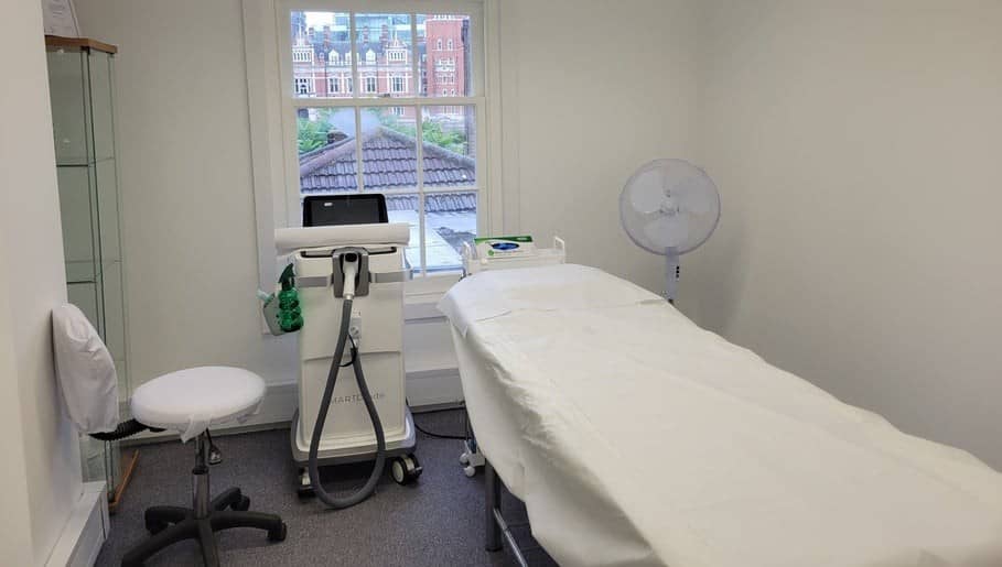 A bright treatment room with a laser machine, a treatment couch and a sash window onto red-brick buildings A bright treatment room with a laser machine, a treatment couch and a sash window onto red-brick buildings
